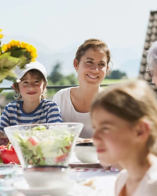 Familie mit Grosseltern essen gemeinsam draussen in der Sonne.